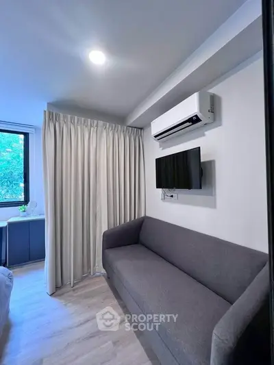 Cozy living room with modern sofa, wall-mounted TV, and air conditioning unit.