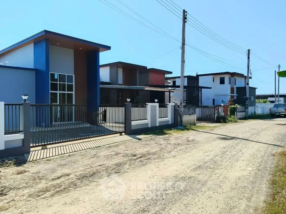 Modern residential street with contemporary houses and gated driveways under clear blue sky.