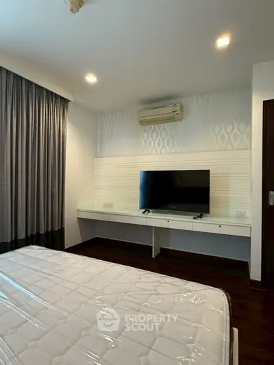 Modern bedroom with wall-mounted TV and air conditioning unit, featuring elegant lighting and dark curtains.
