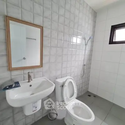 Modern bathroom with sleek fixtures and tiled walls, featuring a shower and a window for natural light.