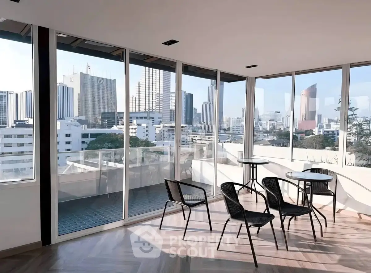 Stunning city view from modern apartment with floor-to-ceiling windows and stylish balcony seating.