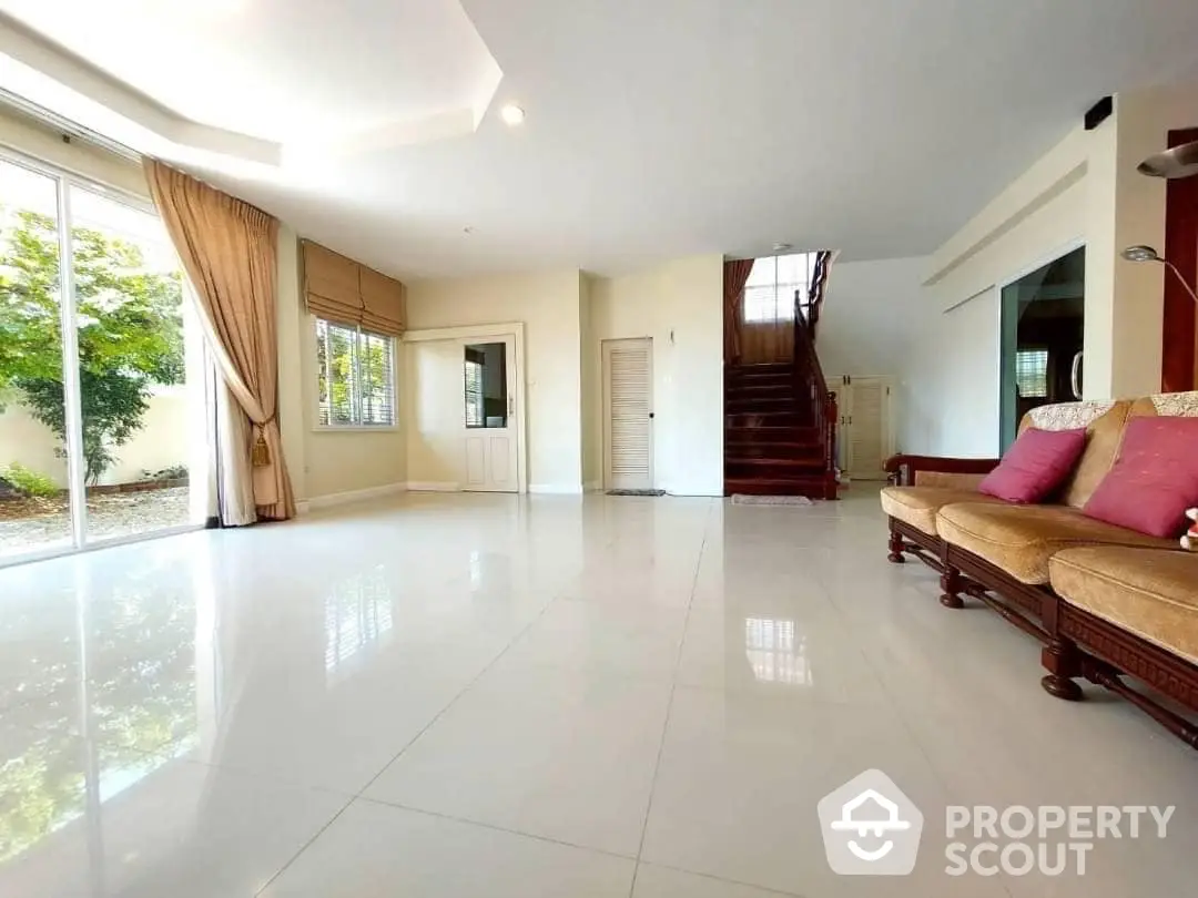 Spacious living room with gleaming tiled floors, large windows, and an elegant staircase leading to the upper level, perfect for luxurious living.