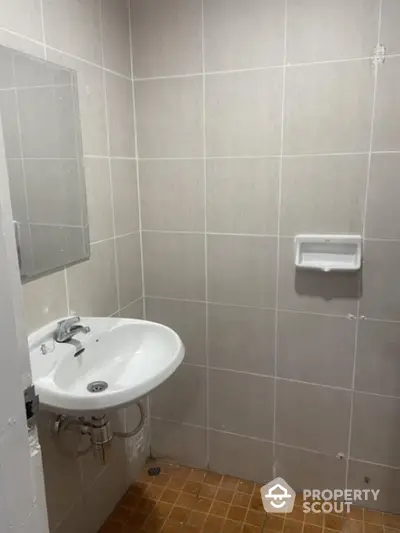 Compact bathroom with wall-mounted sink, tiled walls, and terracotta floor tiles, awaiting personal touches and modern upgrades.