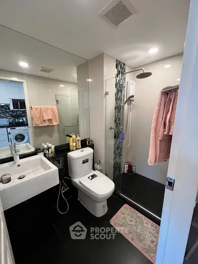 Modern bathroom with glass shower, sleek fixtures, and washing machine in a stylish apartment.