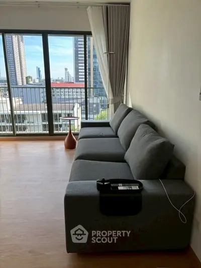 Modern living room with gray sofa and city view balcony in high-rise apartment.