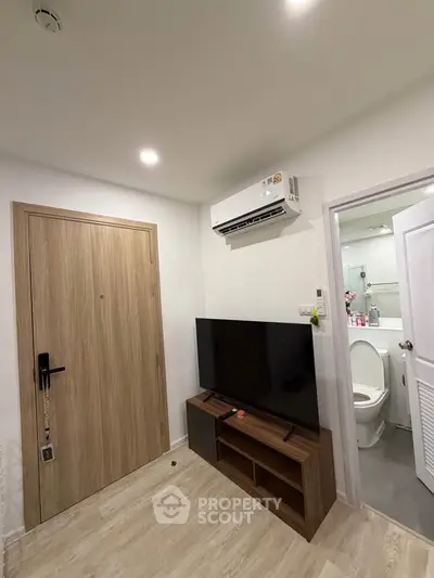 Modern apartment interior with sleek TV setup and bathroom access, showcasing efficient use of space.