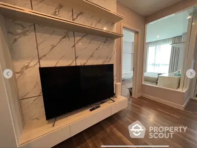 Elegant living room with polished hardwood floors and a custom-built marble TV wall unit, leading to a sunlit balcony with a view.