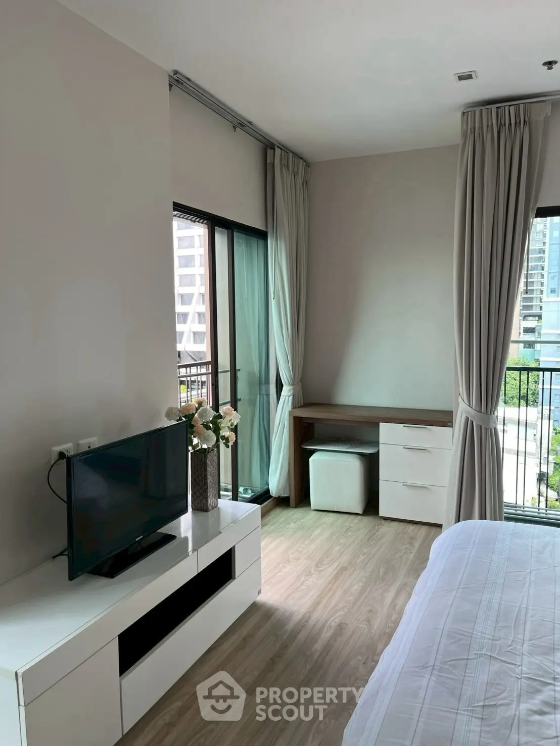 Modern bedroom with balcony view, featuring sleek furniture and natural light in a high-rise apartment.
