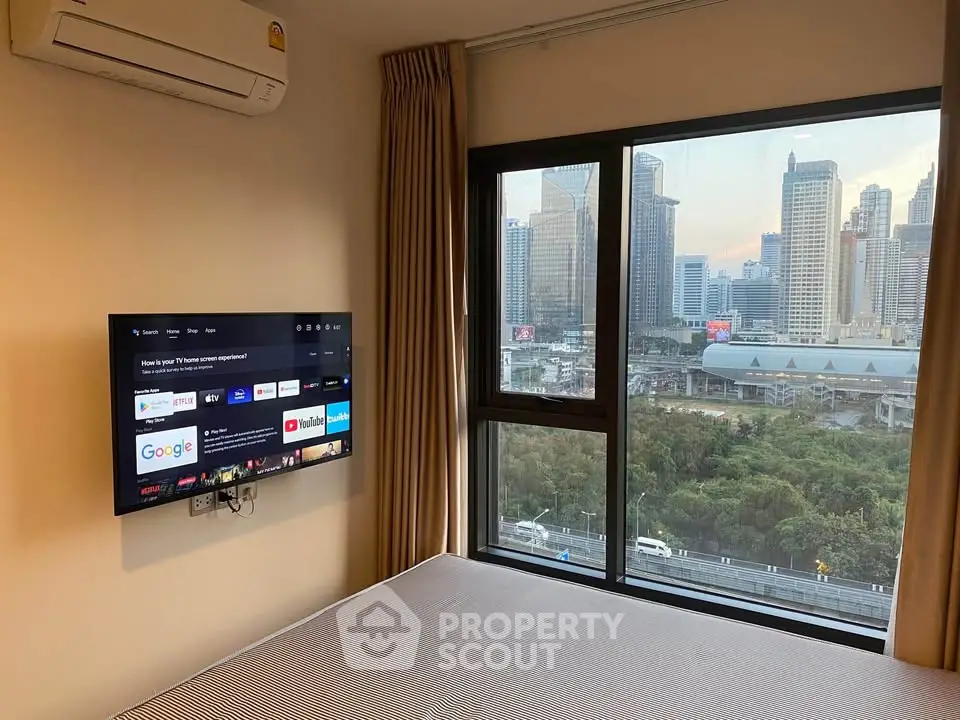 Modern bedroom with city view, wall-mounted TV, and air conditioning in urban apartment.