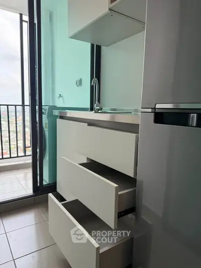 Modern kitchen with sleek cabinetry and balcony view, featuring a stainless steel fridge and ample storage space.