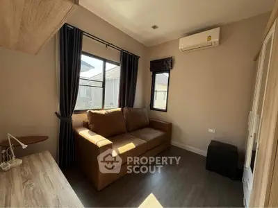 Cozy living room with sofa and air conditioning, featuring natural light and modern decor.