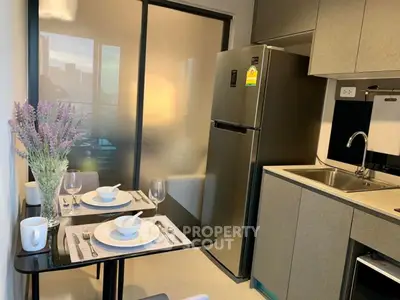 Modern compact kitchen with dining area, featuring sleek cabinets and stainless steel fridge.