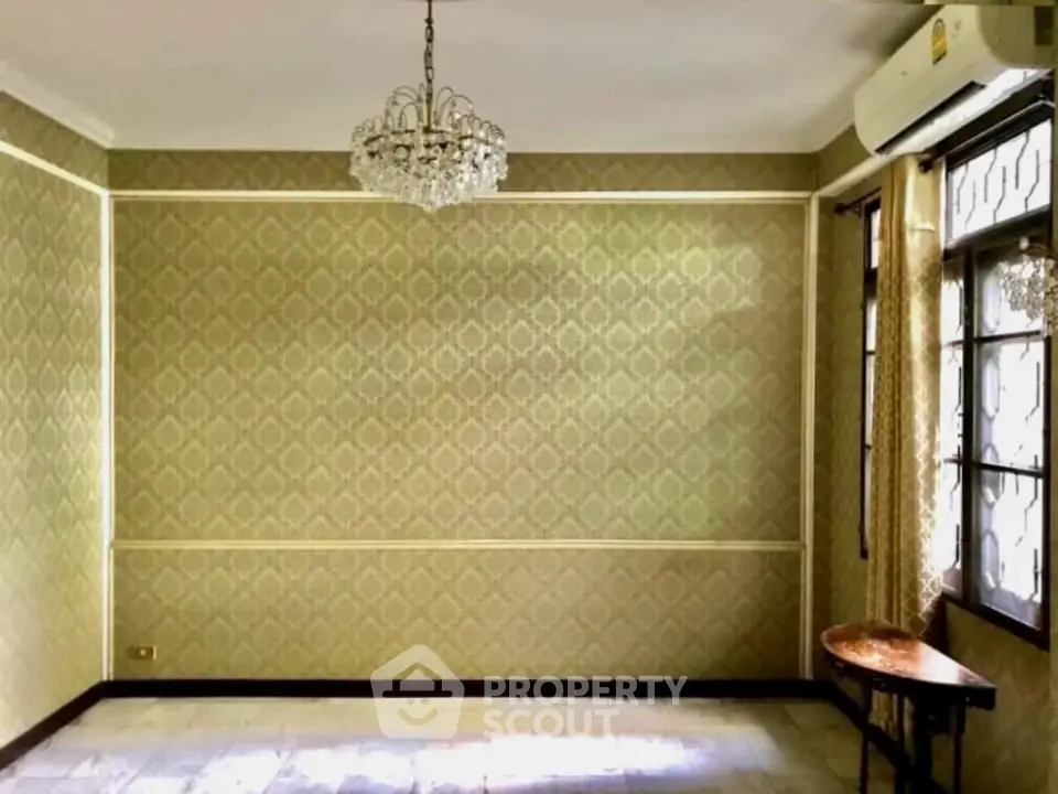 Elegant living room with chandelier and vintage wallpaper, featuring large windows and air conditioning.