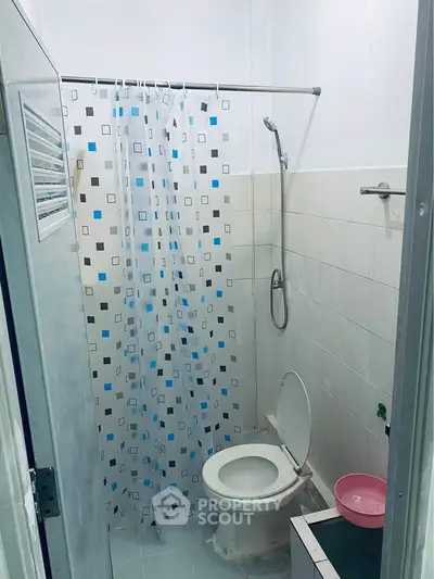 Compact bathroom with shower and toilet, featuring a patterned curtain and tiled walls.