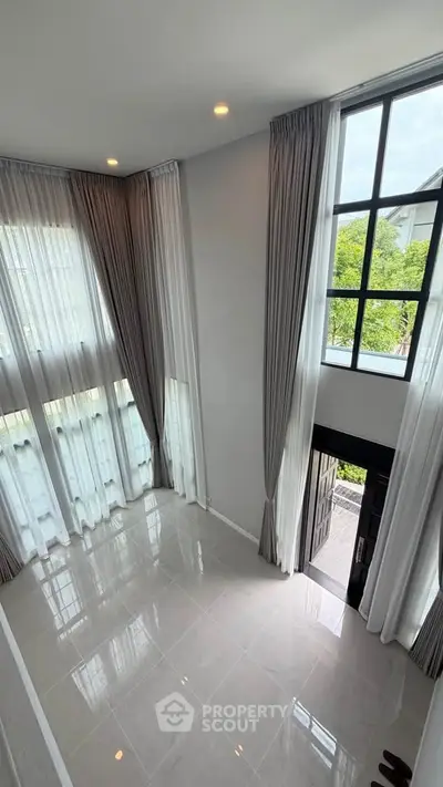 Spacious modern living room with high ceilings and large windows offering natural light and garden view.