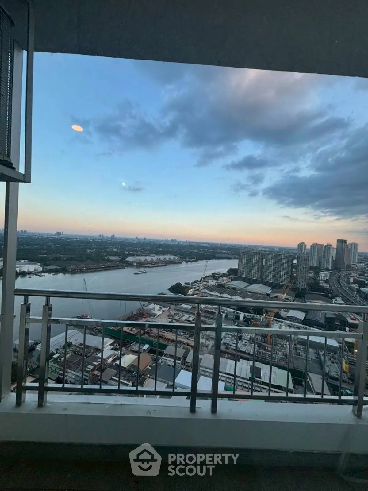 Stunning high-rise balcony view overlooking river and cityscape at sunset.