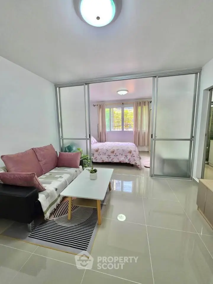 Modern living room with glass partition leading to a cozy bedroom, featuring sleek tile flooring and stylish decor.