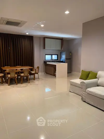 Spacious open-plan living room with modern kitchen and dining area, featuring sleek tile flooring and cozy seating.