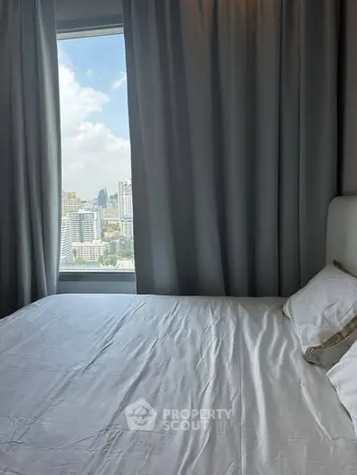 Cozy bedroom with city view through large window, featuring elegant curtains and a comfortable bed.