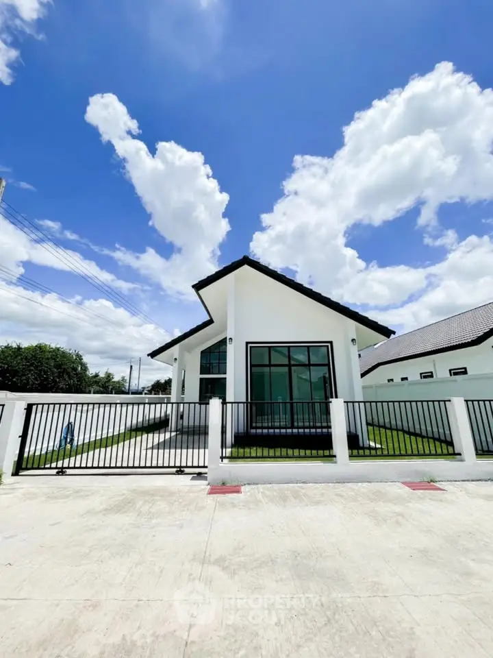 Modern single-story house with sleek design and large windows, surrounded by a white fence under a clear blue sky.