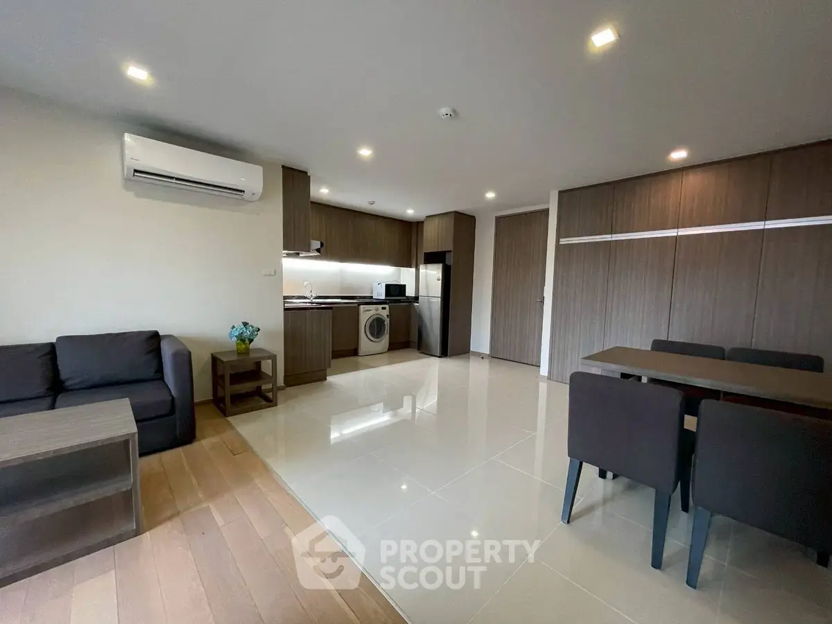 Modern open-plan living room with kitchen, dining area, and washing machine, featuring sleek wooden cabinetry.