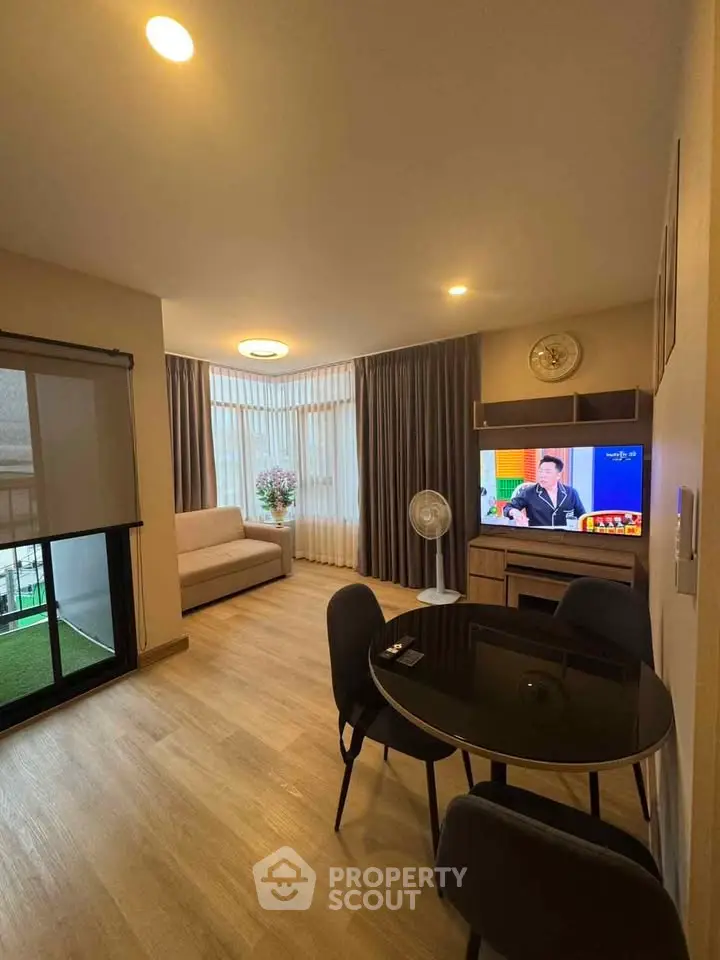 Modern living room with cozy seating and natural light, featuring a TV and dining area.