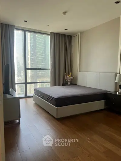 Spacious bedroom with large window offering city views, featuring modern furnishings and elegant decor.