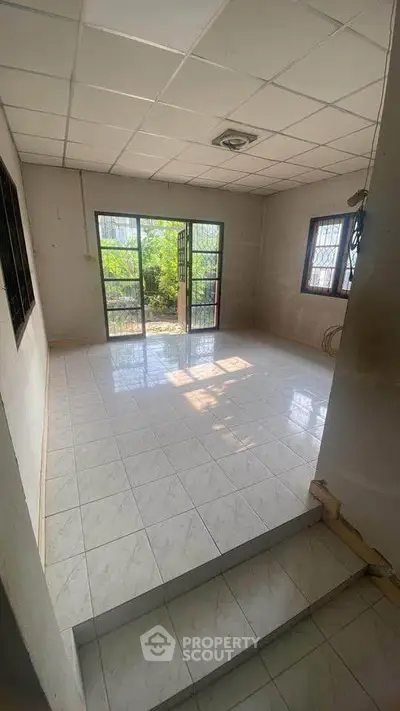 Spacious room with tiled flooring and large windows offering natural light and garden view.