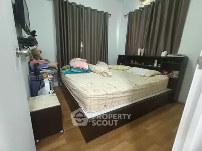Cozy bedroom with wooden flooring and large bed, featuring ample natural light from curtained windows.