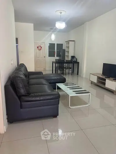 Spacious living room with modern black leather sofa and sleek dining area, perfect for entertaining.