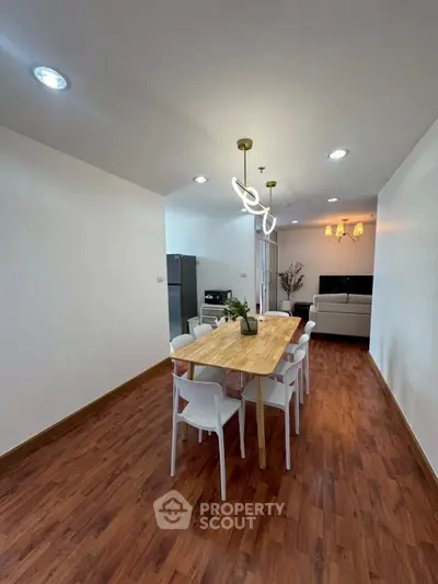 Spacious dining area with modern lighting and wooden flooring in open-plan apartment.