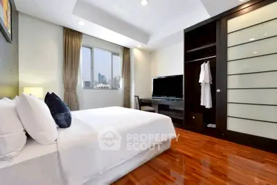 Luxurious bedroom with sleek wooden flooring and city view, featuring a modern TV setup and spacious wardrobe.