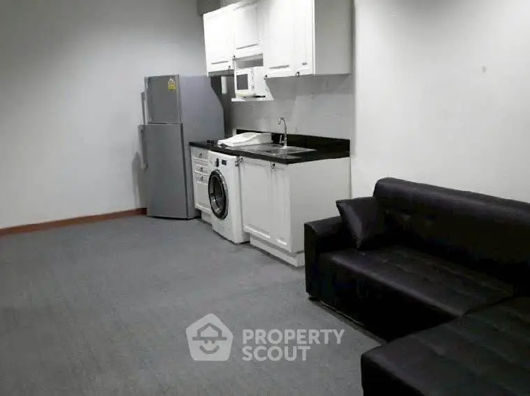 Compact studio apartment with modern kitchen and cozy living area, featuring a washing machine and fridge.