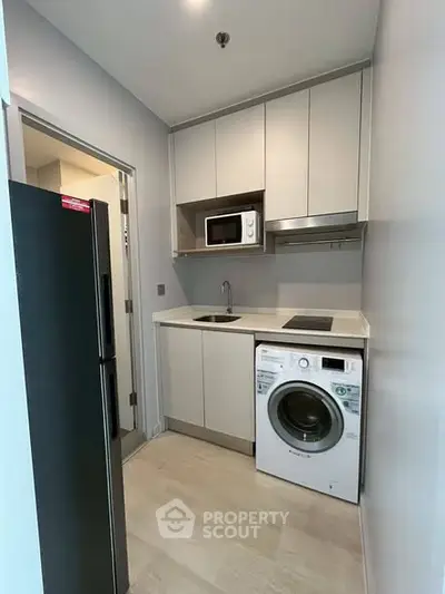 Modern compact kitchen with washing machine and microwave in sleek apartment.