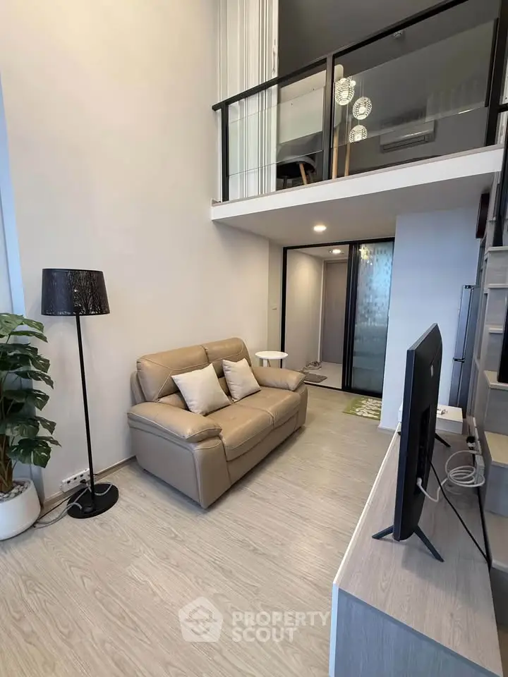 Modern loft-style living room with high ceiling and mezzanine, featuring sleek furniture and contemporary decor.
