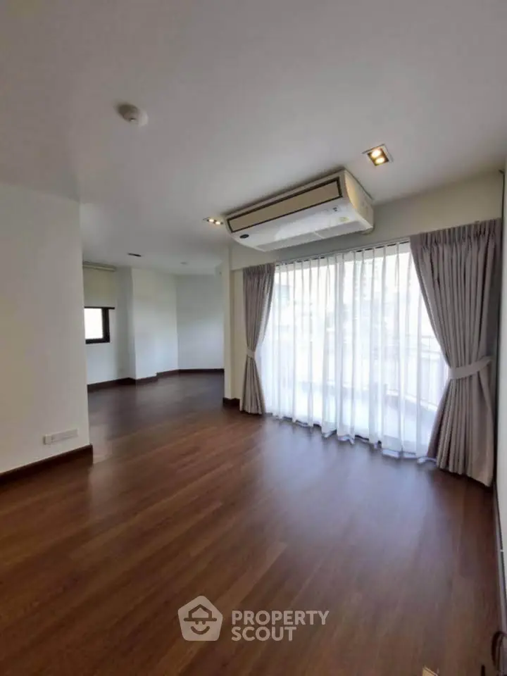 Spacious living room with large windows and elegant curtains, featuring a modern air conditioning unit.