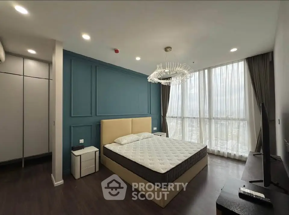 Luxurious bedroom with modern chandelier and floor-to-ceiling windows offering stunning city views.