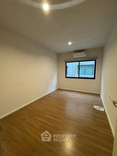 Spacious empty room with wooden flooring and air conditioning, ideal for customization.