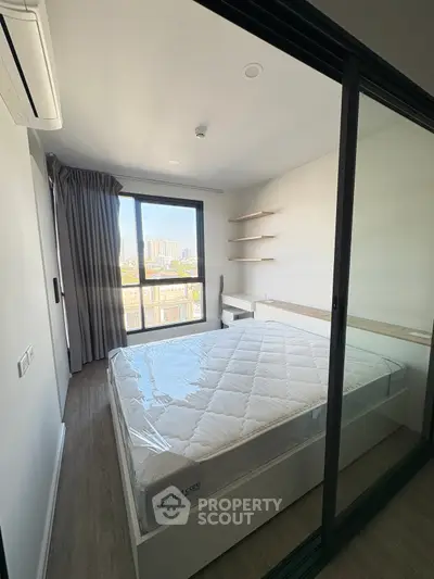 Modern bedroom with large window and city view, featuring a comfortable bed and sleek design.
