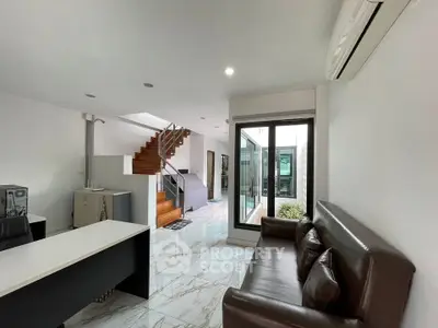 Modern living room with sleek staircase and glass door leading to outdoor area.
