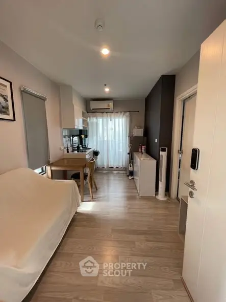 Modern living room with open kitchen, wooden flooring, and natural light.