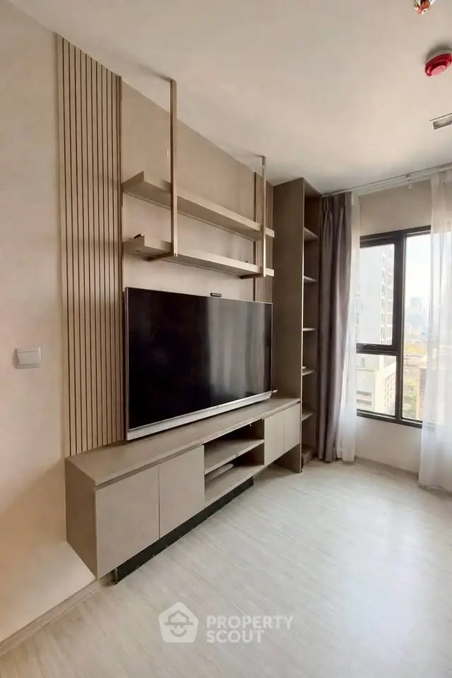 Modern living room with sleek TV unit and large window offering city views.