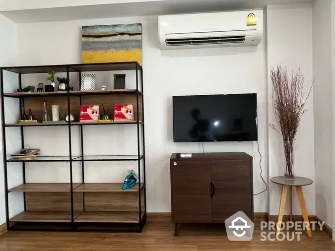 Cozy living room interior with modern furniture, flat-screen TV, and air conditioning unit, complemented by warm wooden flooring and tasteful decor.