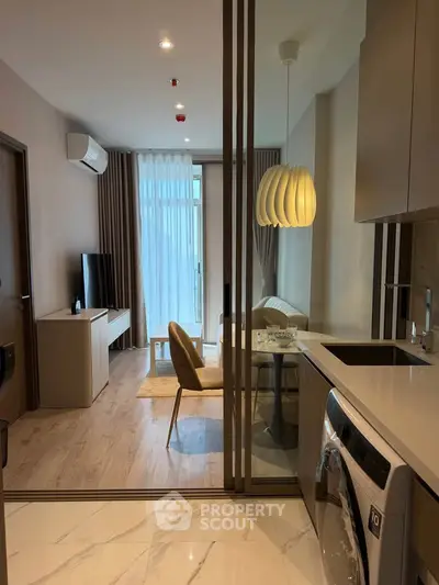 Modern apartment interior with open kitchen and cozy living area, featuring stylish lighting and a washing machine.