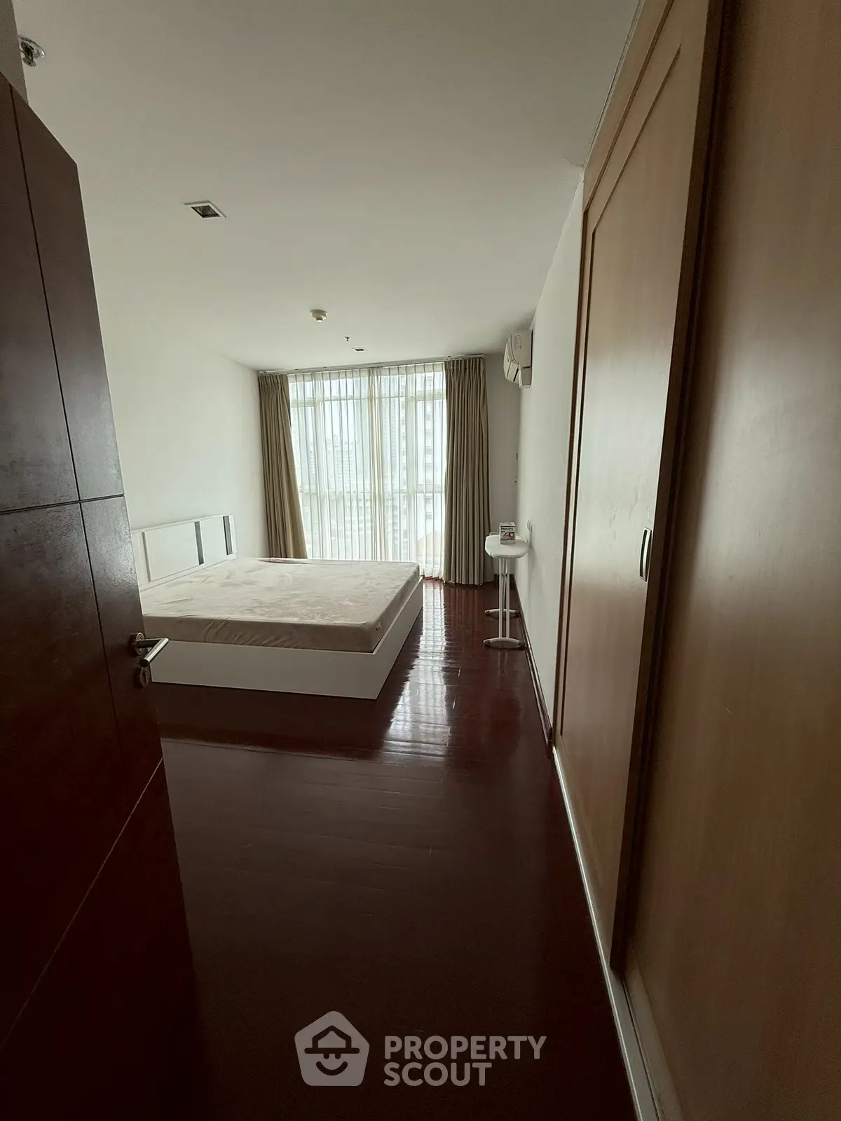 Spacious bedroom with large window and wooden flooring, offering ample natural light and cozy ambiance.