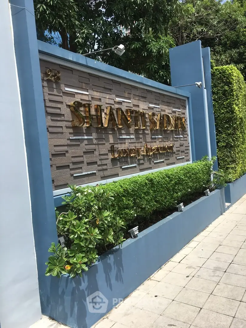 Elegant entrance sign of luxury apartment complex with lush greenery and modern design.