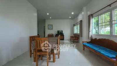 Spacious living room with dining area and natural light, featuring wooden furniture and tiled flooring.