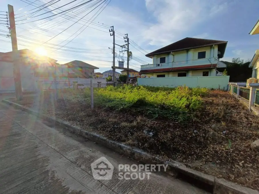 Vacant land plot in suburban neighborhood with clear sky and residential houses nearby.