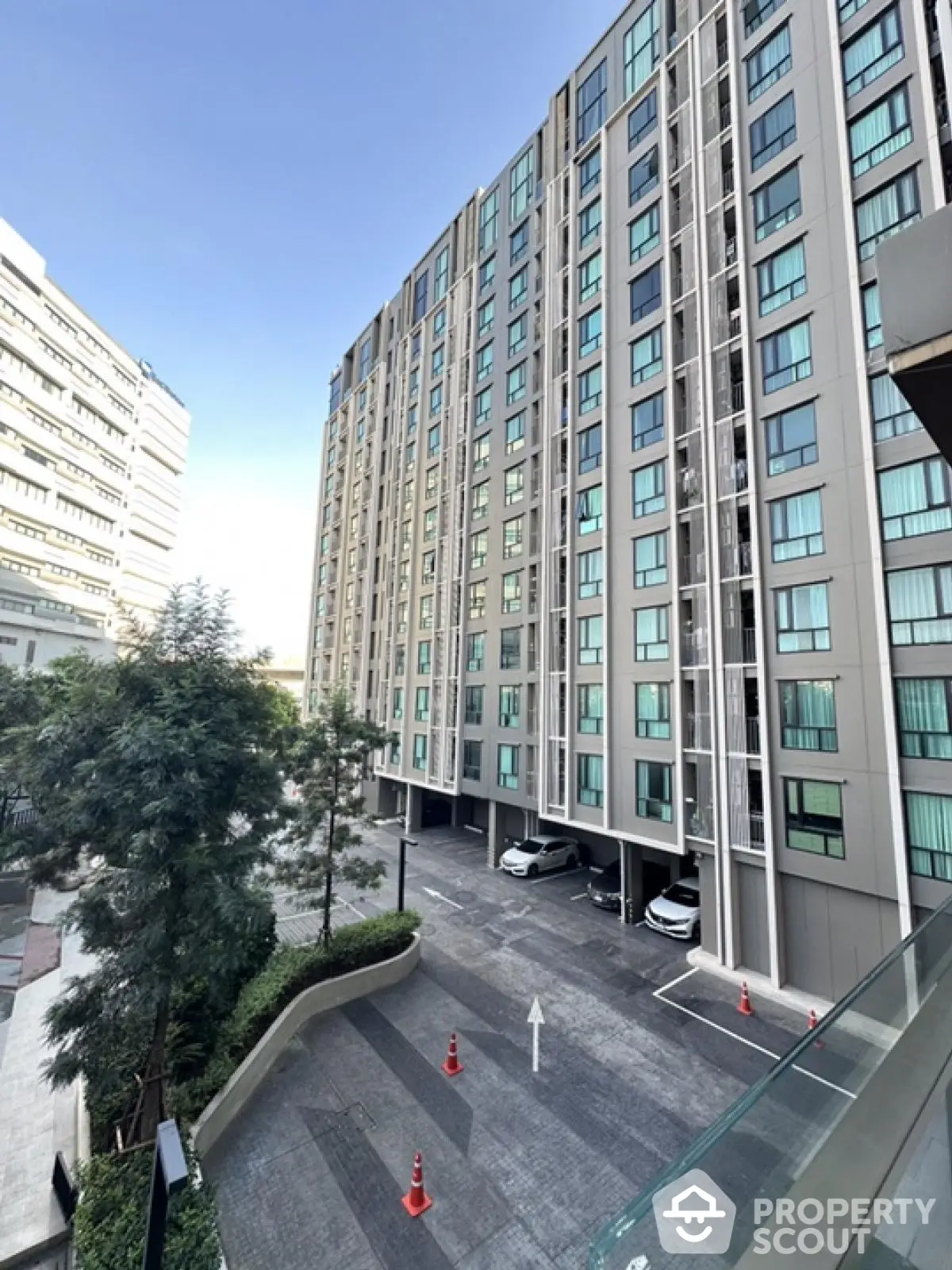 Modern high-rise apartment building with spacious parking area and lush greenery