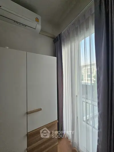 Bright bedroom corner with modern wardrobe and large window with sheer curtains.